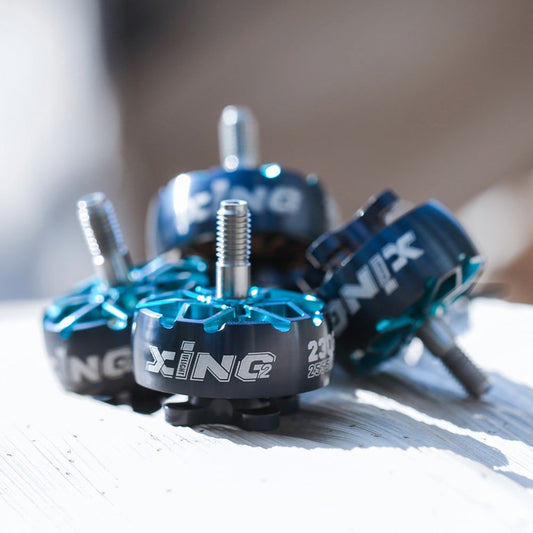 Four turquoise iFlight XING2 brushless FPV motors photographed on a wooden surface